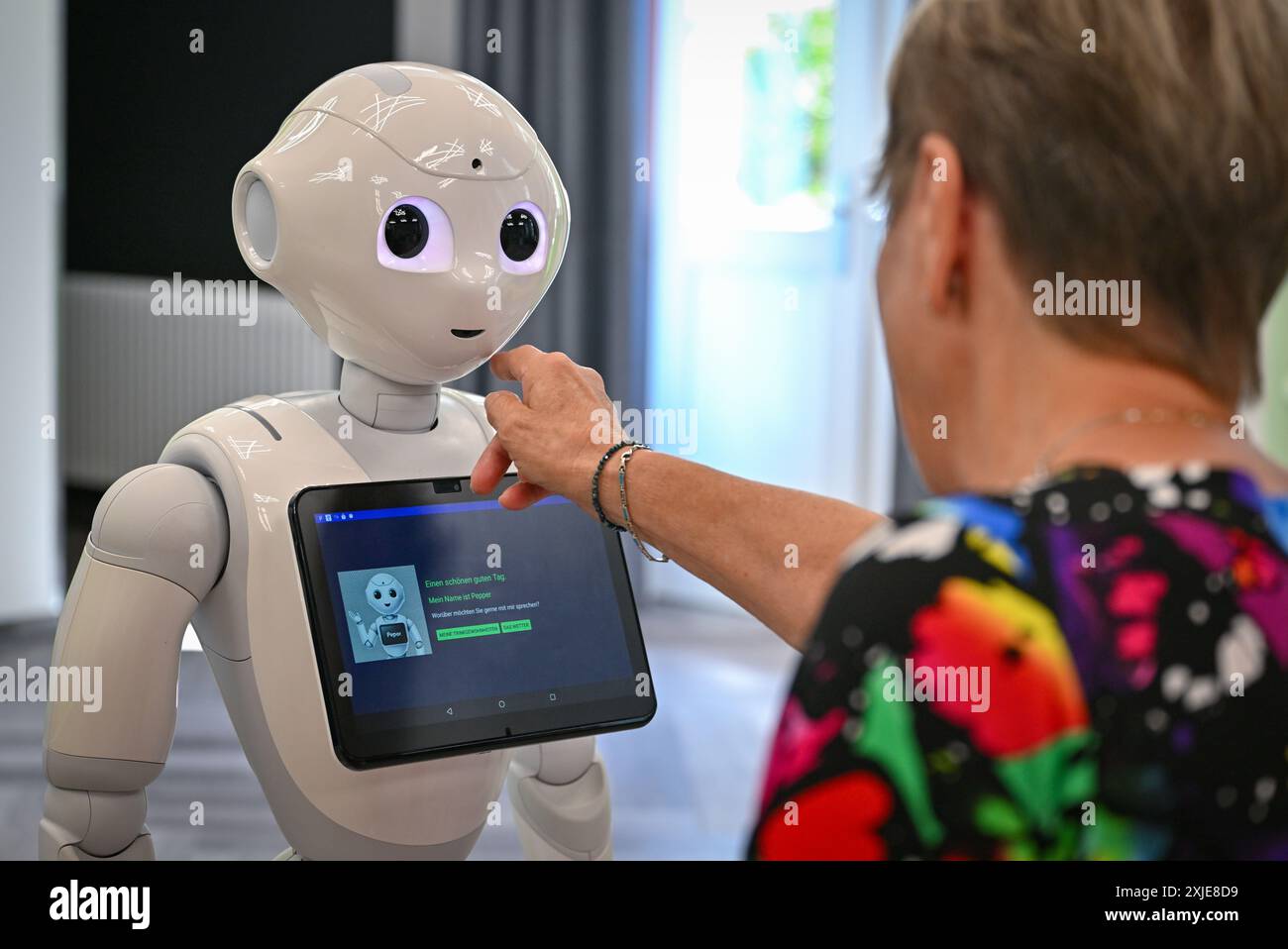 Cottbus, Germania. 18 luglio 2024. Un'interazione in tempo reale tra un paziente simulato e un robot può essere vista durante un evento stampa presso il Carl-Thiem-Klinikum Cottbus. Attualmente è in corso uno studio pilota presso la Brandenburg University of Technology Cottbus-Senftenberg (BTU) per studiare gli effetti delle modalità di interazione di un robot sociale (Pepper) sull'impegno e sulla percezione dei soggetti sottoposti a test in situazioni di assistenza tipiche. Crediti: Patrick Pleul/dpa/Alamy Live News Foto Stock