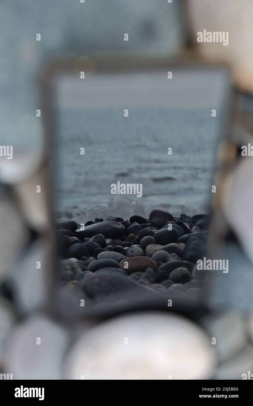 Smartphone con riflesso del mare sullo sfondo delle pietre Foto Stock