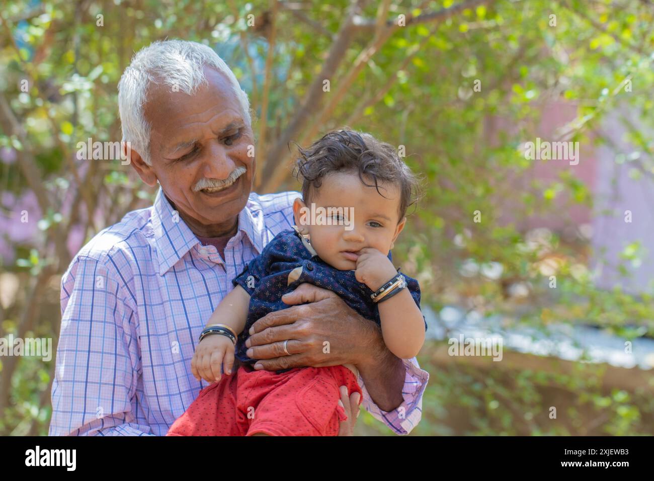 Nonno felice che tiene il suo nipote indiano in un parco. La scena cattura un tenero momento di amore, gioia e amicizia. Foto Stock