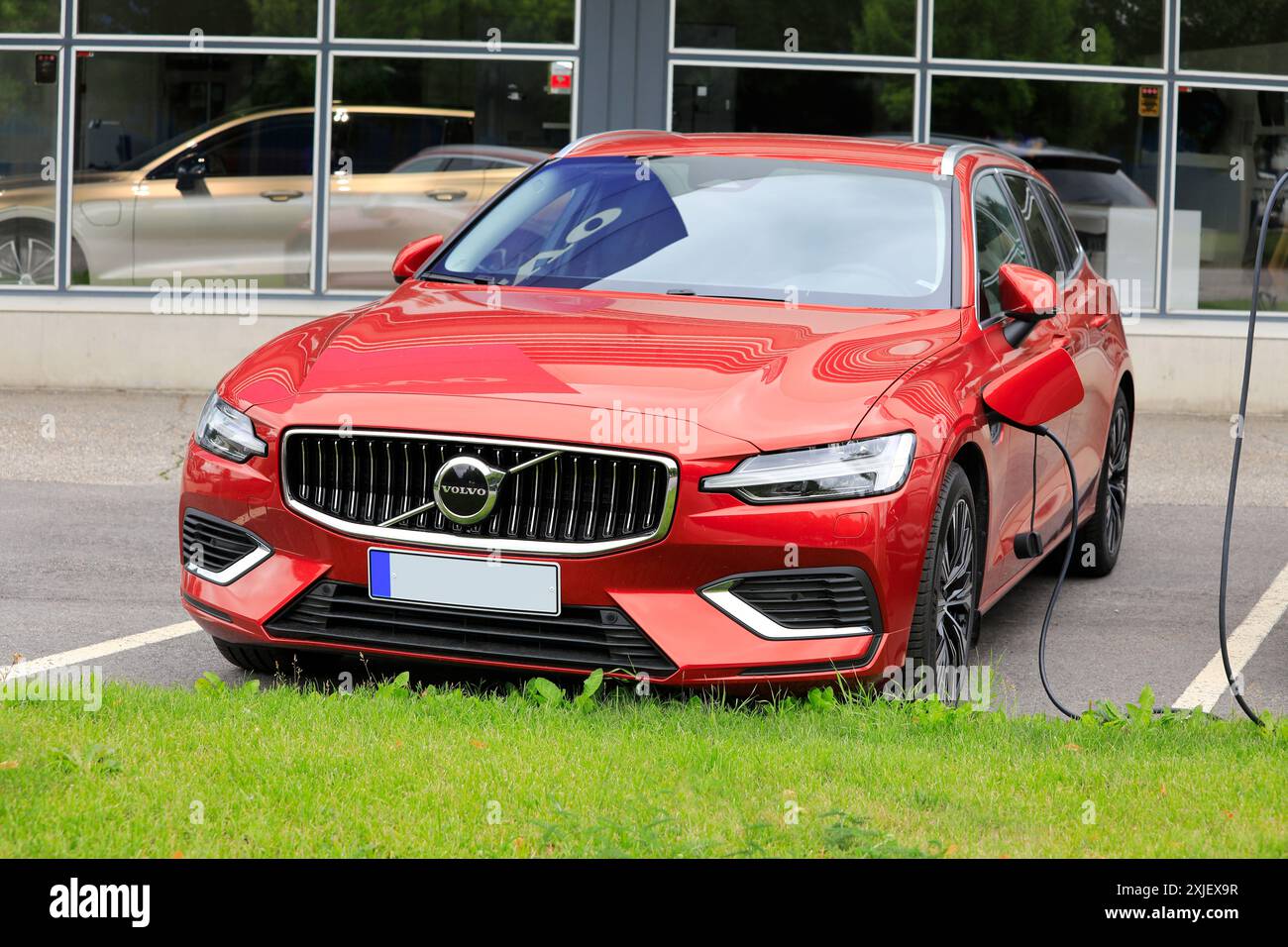 Auto elettrica ibrida rossa Volvo V60 (II) AWD 2024 collegata al caricabatteria presso la concessionaria di Salo, Finlandia. 14 luglio 2024. Foto Stock