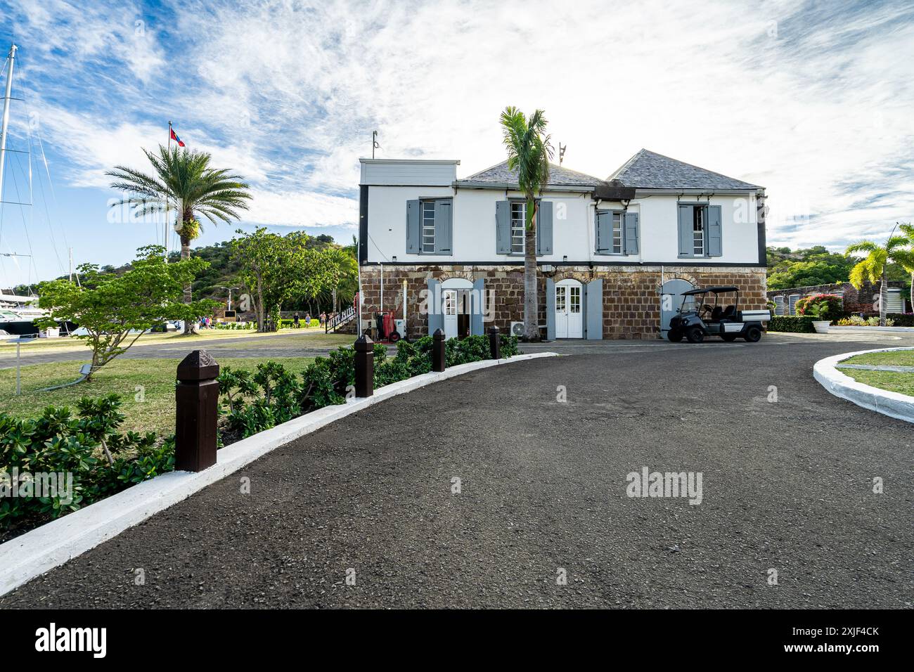 Dettagli del giardino e dell'edificio storico nel cantiere navale di Nelson nel porto inglese di Antigua, in una giornata di sole con palme e barche a vela al molo Foto Stock