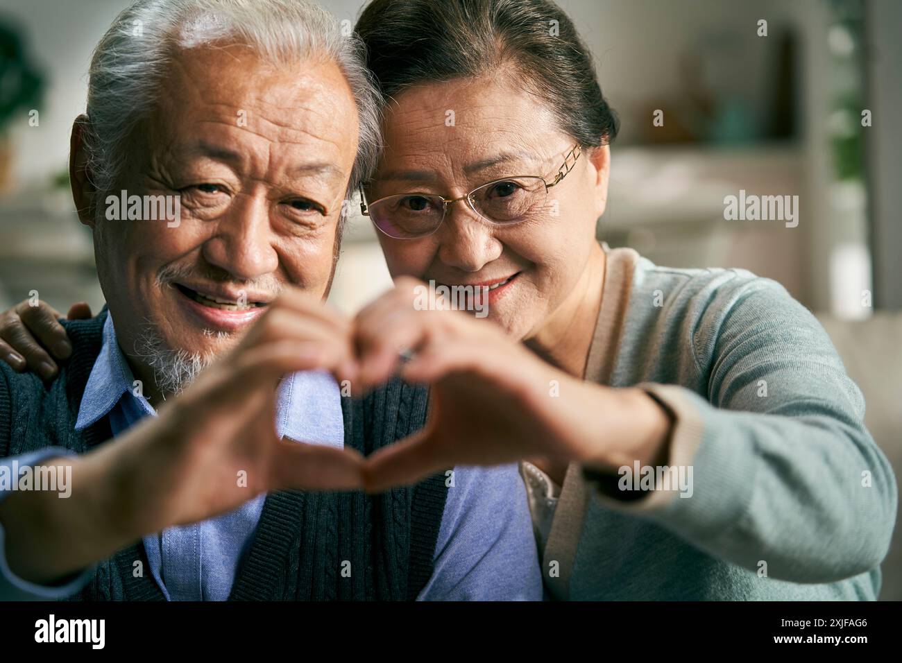 felice coppia asiatica senior che si forma a forma di cuore con la mano mentre chiacchiera con amici e familiari Foto Stock