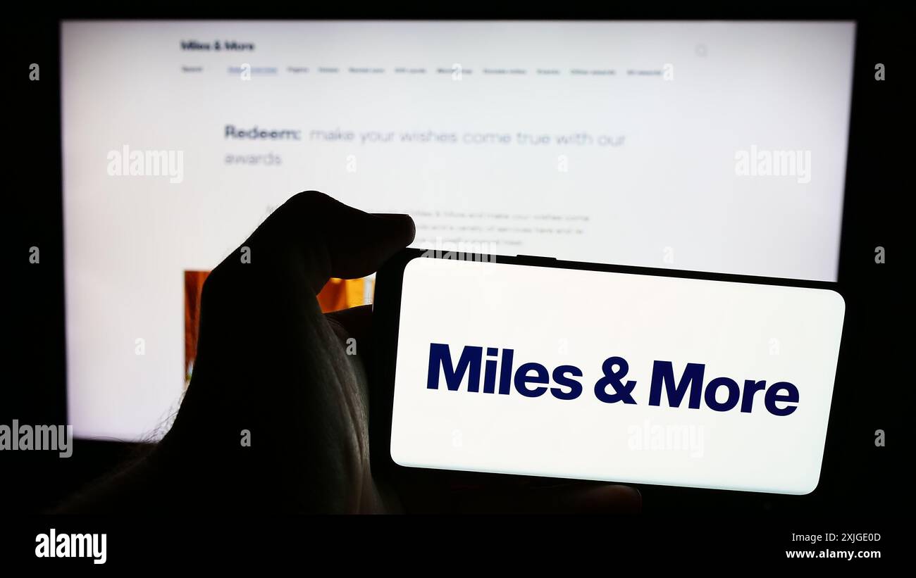 Persona con smartphone con logo del programma frequent flyer Miles and More (Lufthansa) davanti al sito Web. Mettere a fuoco il display del telefono. Foto Stock