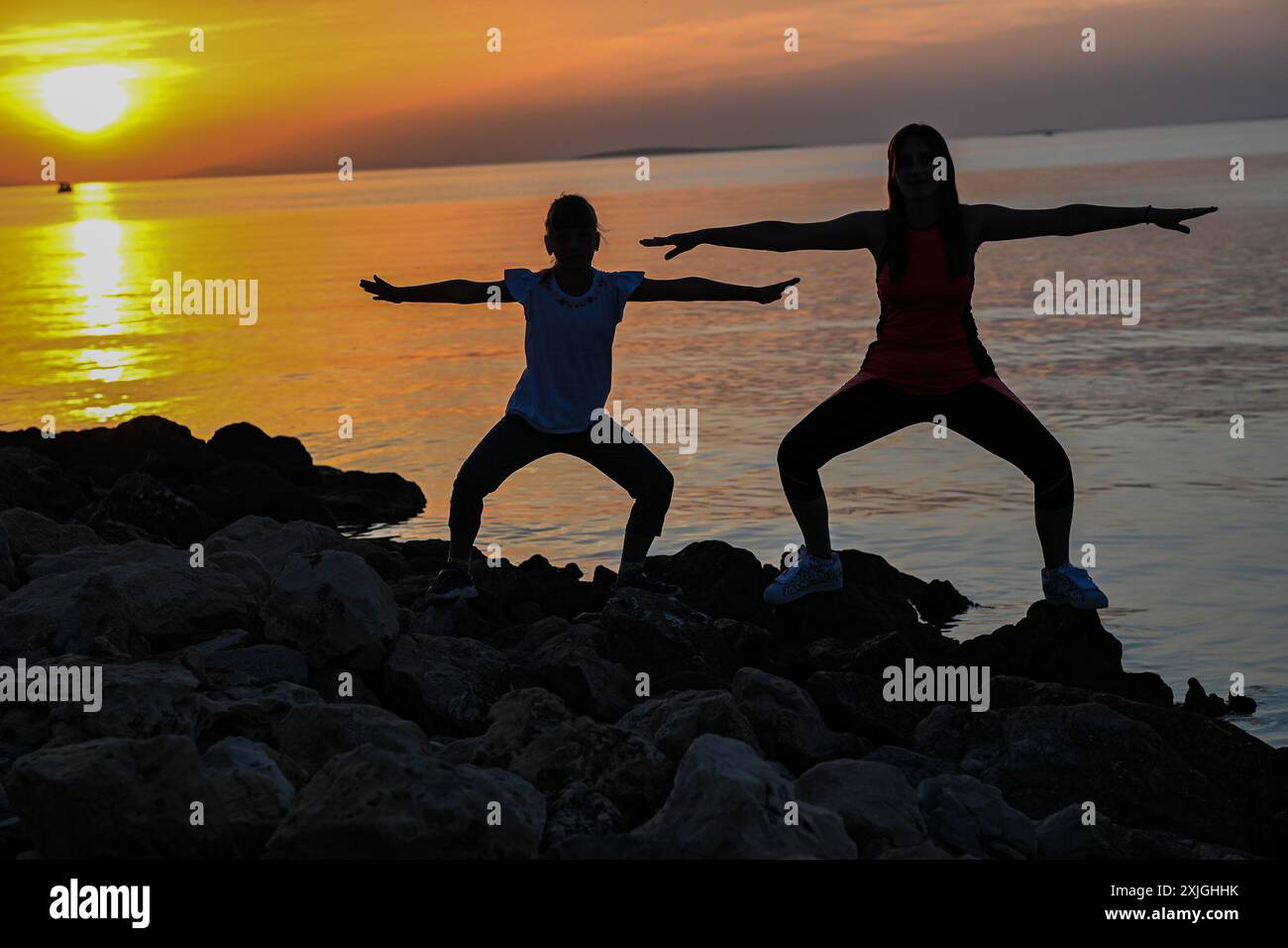 Madre e figlia praticano yoga sulla spiaggia al tramonto, godendosi un momento di pace insieme. Foto Stock