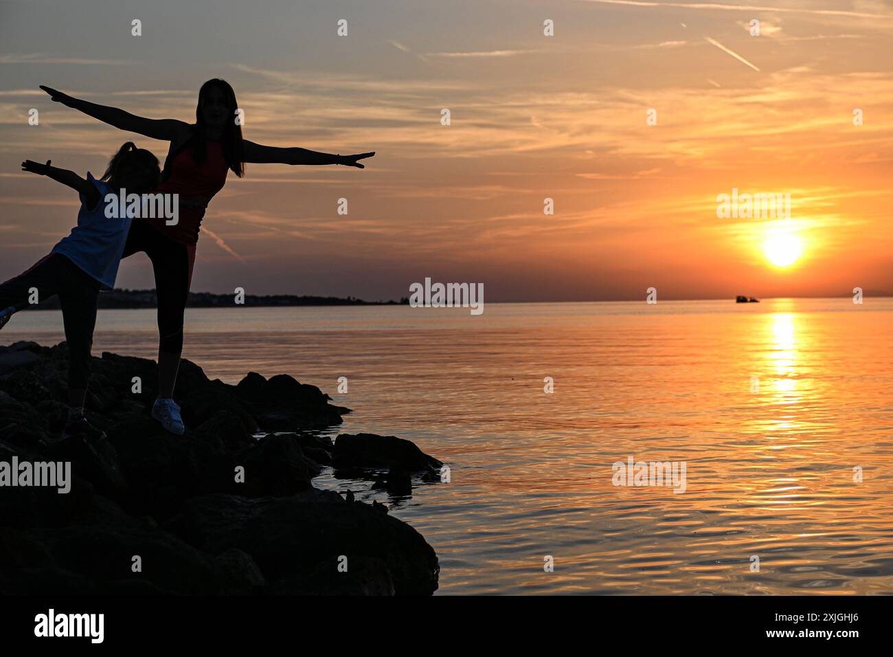 Madre e figlia praticano yoga sulla spiaggia al tramonto, godendosi un momento di pace insieme. Foto Stock