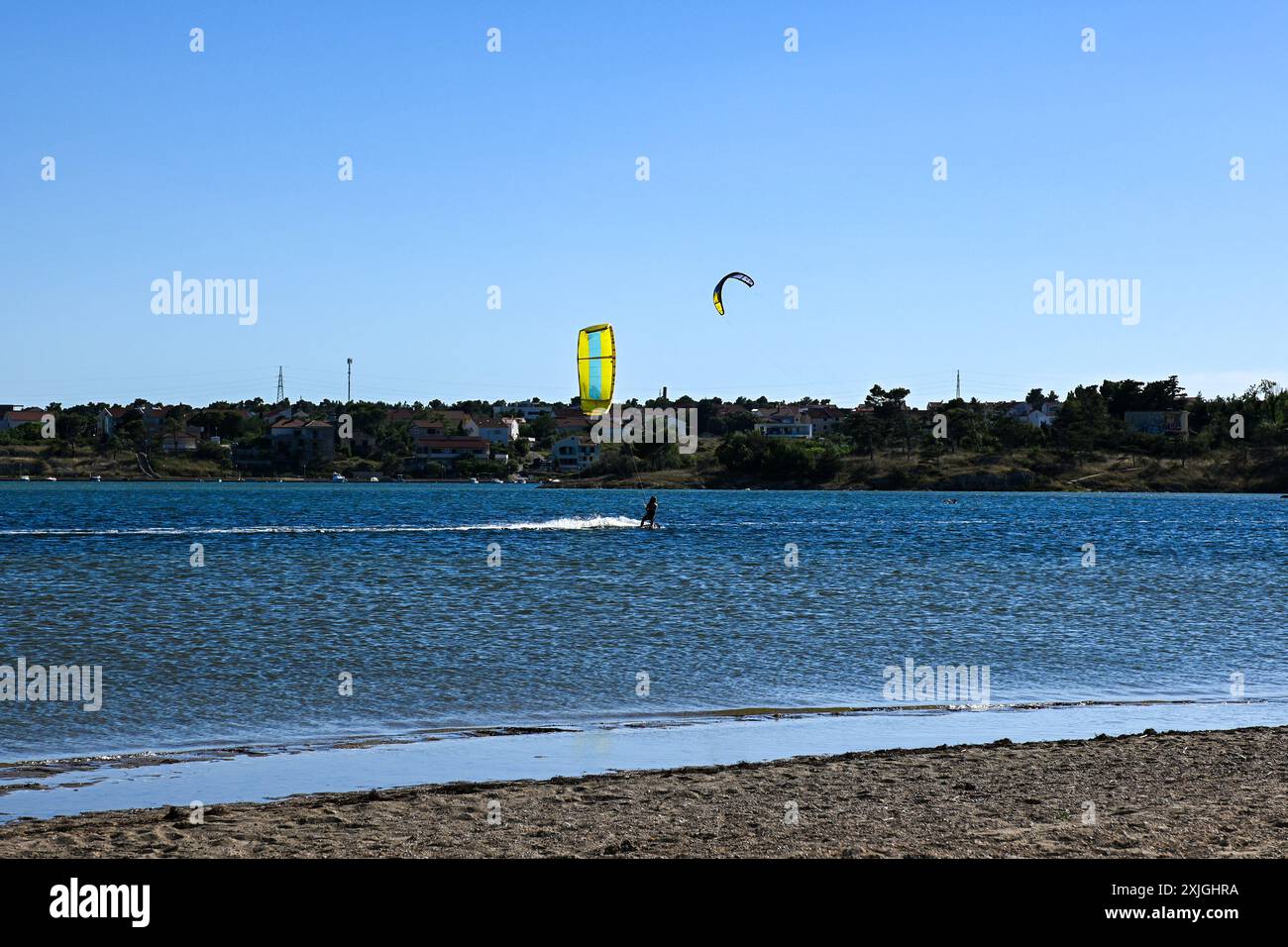 Kitesurfer sta cavalcando un'onda in una giornata di sole con il cielo blu. Foto Stock