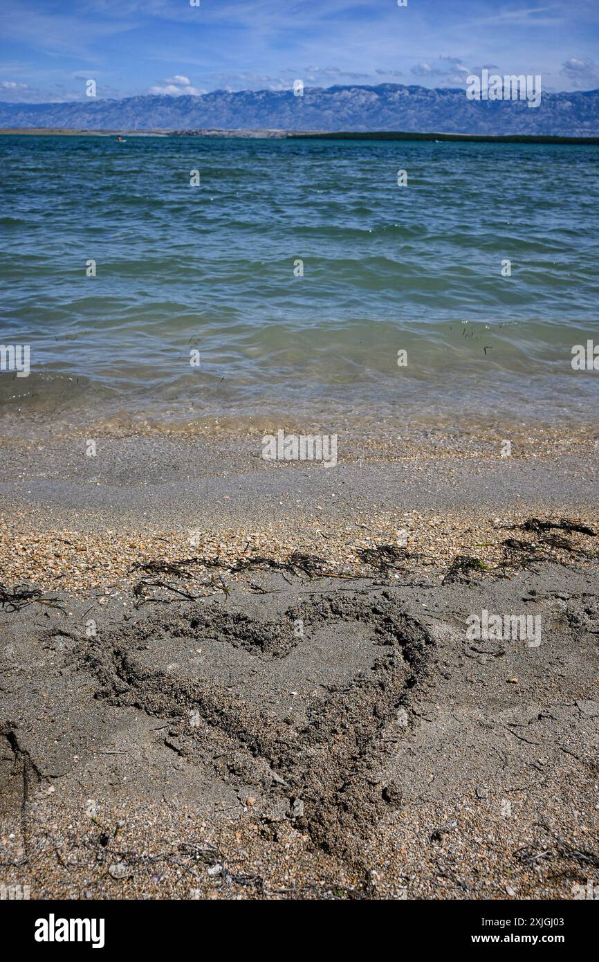 Cuore disegnato nella sabbia di una spiaggia che viene spazzato via dalle onde dell'oceano, rappresentando l'amore perduto. Foto Stock