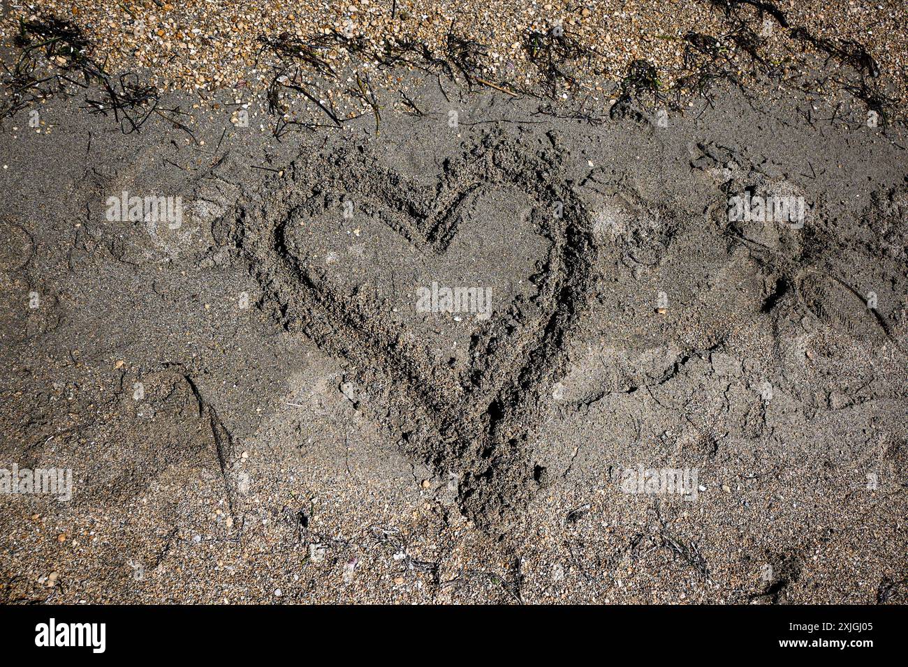 Cuore disegnato nella sabbia di una spiaggia che viene spazzato via dalle onde dell'oceano, rappresentando l'amore perduto. Foto Stock