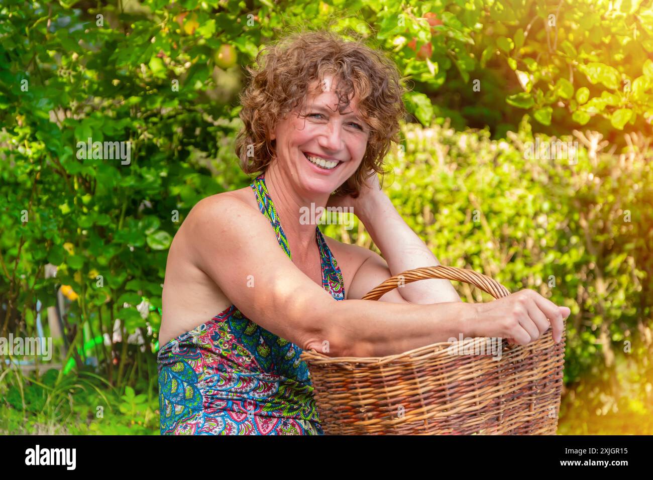 Donna che sorride con un cesto in un giardino Foto Stock
