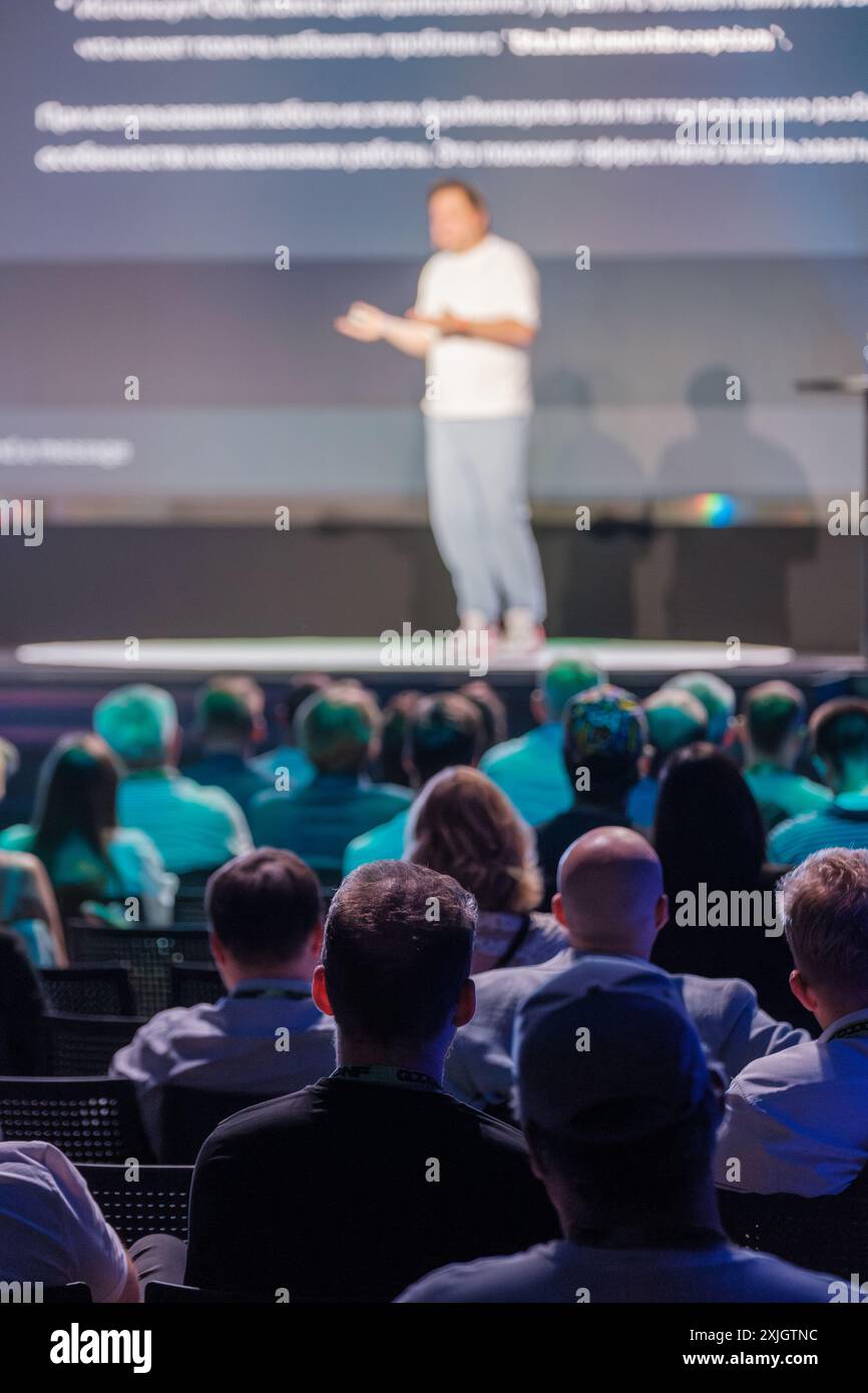 Relatore che presenta sul palco a un pubblico seduto durante una conferenza d'affari. Il pubblico è impegnato e attento. Foto Stock