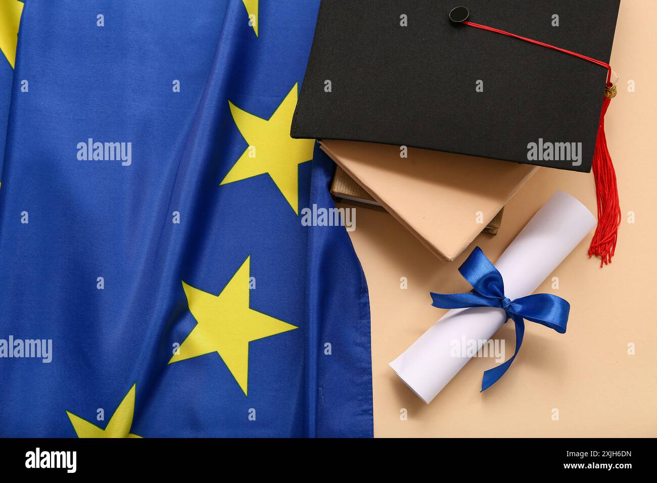 Diploma con nastro blu, libro, bandiera dell'Unione europea e cappello di graduazione su sfondo beige Foto Stock