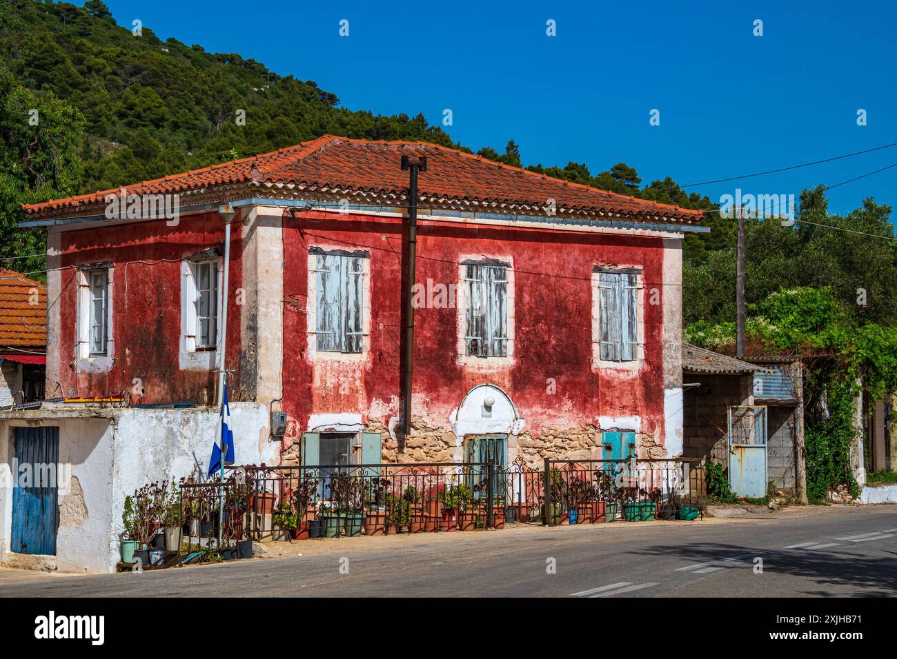 Zante, Grecia - 6 giugno 2024: Pittoresca facciata di una tradizionale casa locale con pareti rosse in pietra e finestre turchesi, vista in atmosfera di Exo Chora Foto Stock