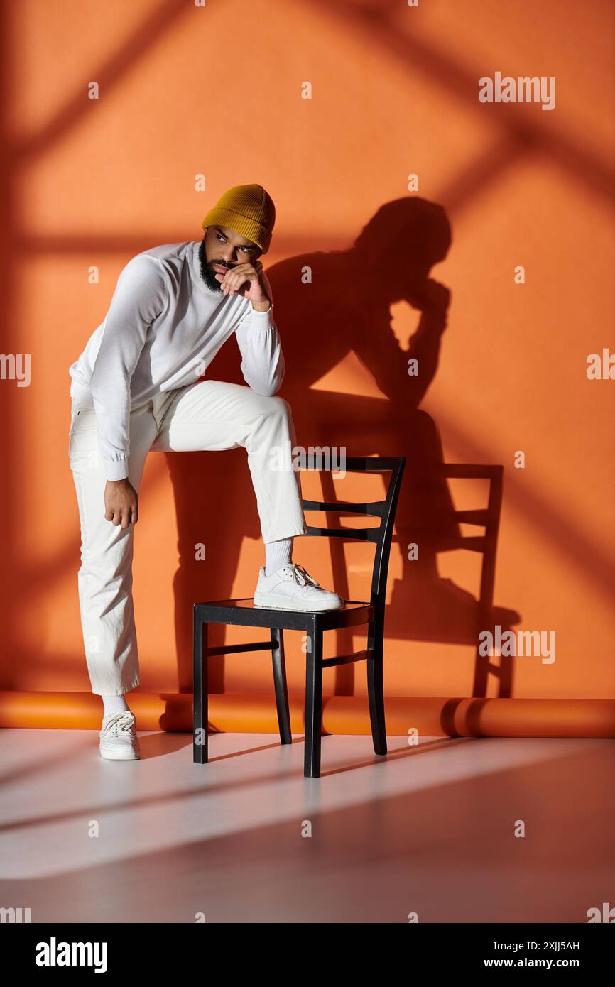 Un elegante uomo afroamericano siede su una sedia in una sala vivace. Foto Stock