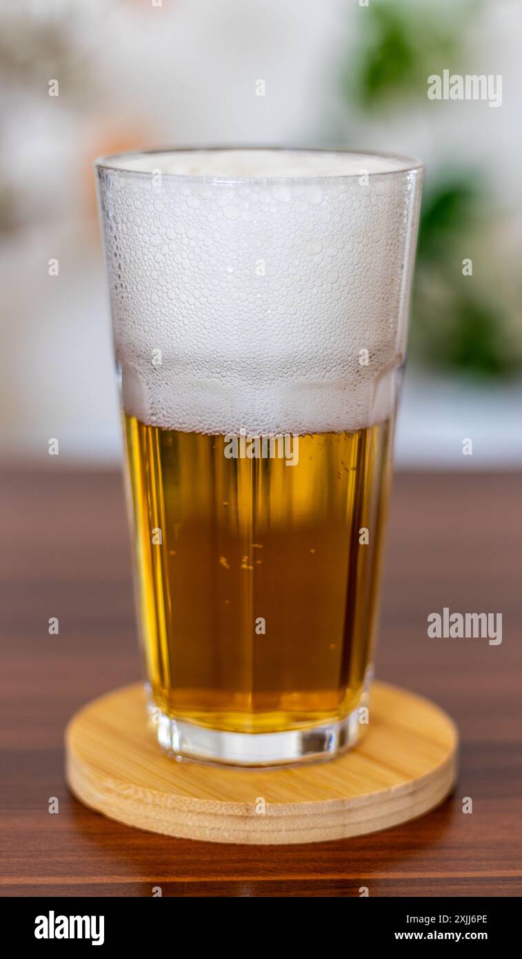 Un bicchiere di birra su un sottobicchiere di legno. Foto Stock