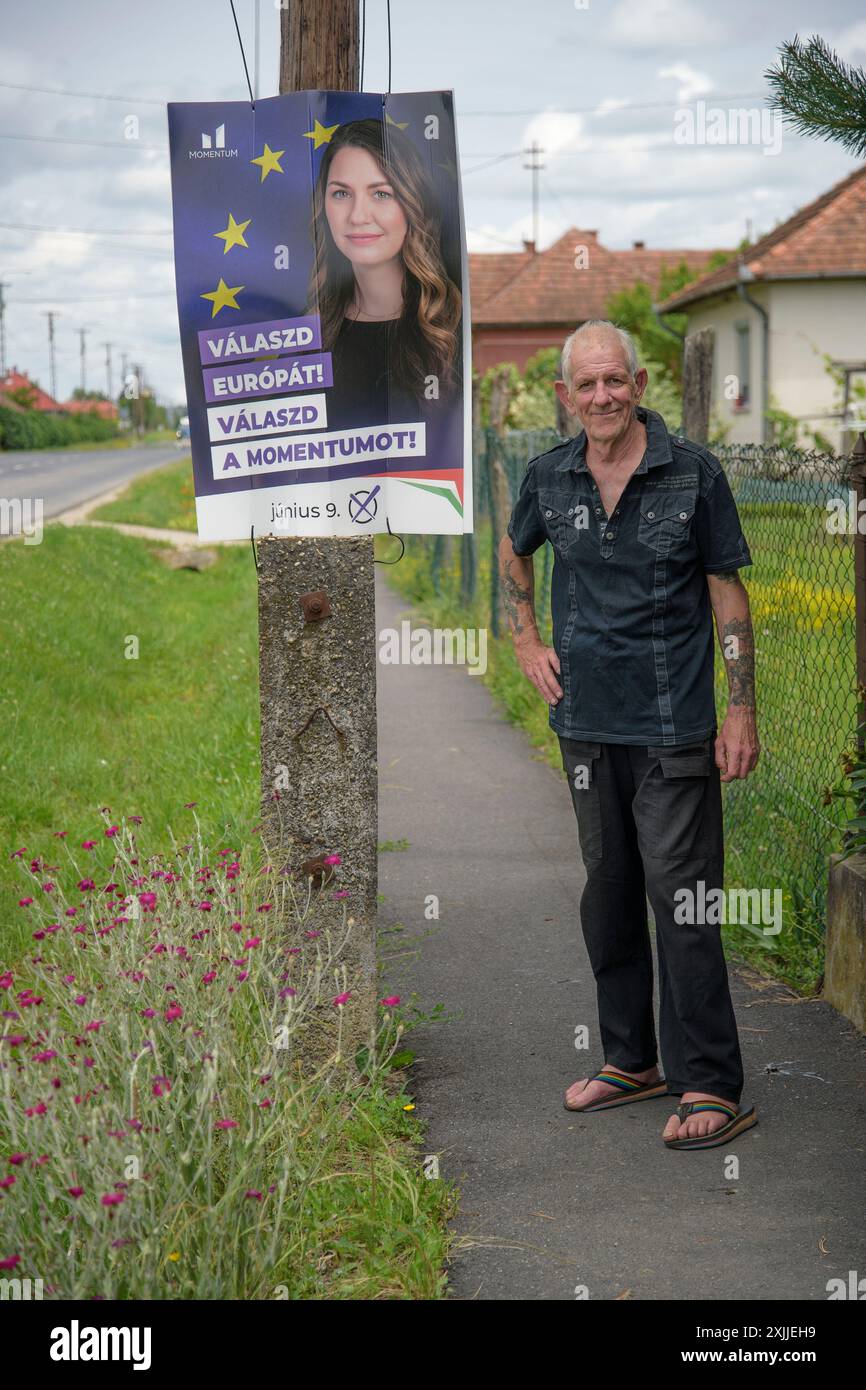 un uomo anziano in piedi accanto al manifesto dei candidati alle elezioni europee nel piccolo villaggio ungherese mentre va al seggio elettorale per esprimere il suo voto Foto Stock