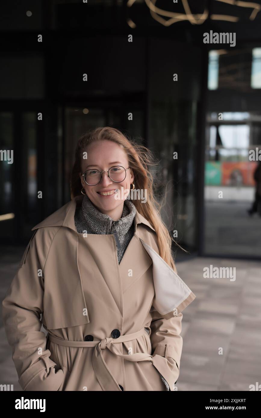 Una donna felice con il cappotto e gli occhiali guarda la macchina fotografica in autunno Foto Stock