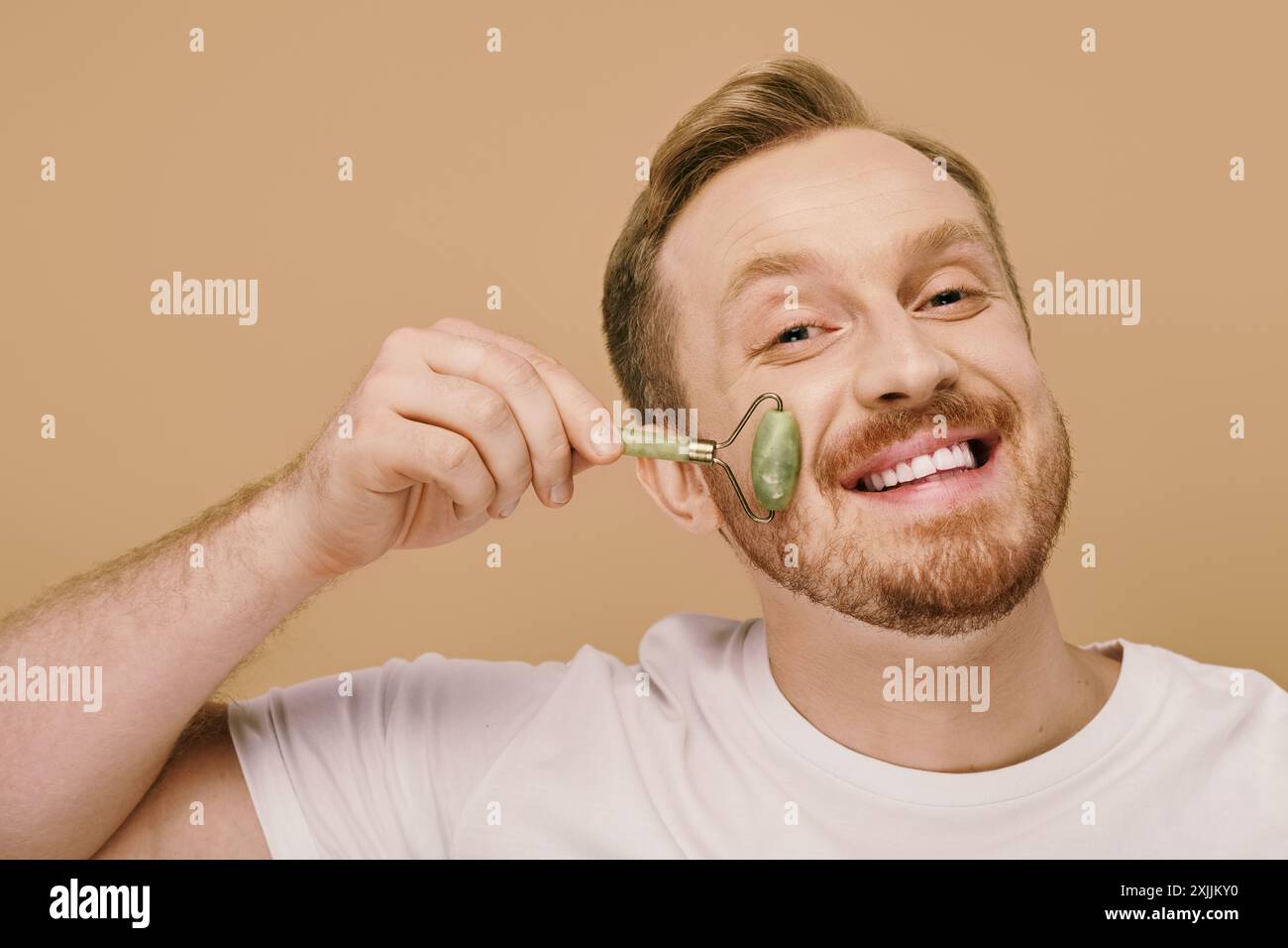 Uomo sorridente in un abbigliamento casual che tiene il face roller. Foto Stock