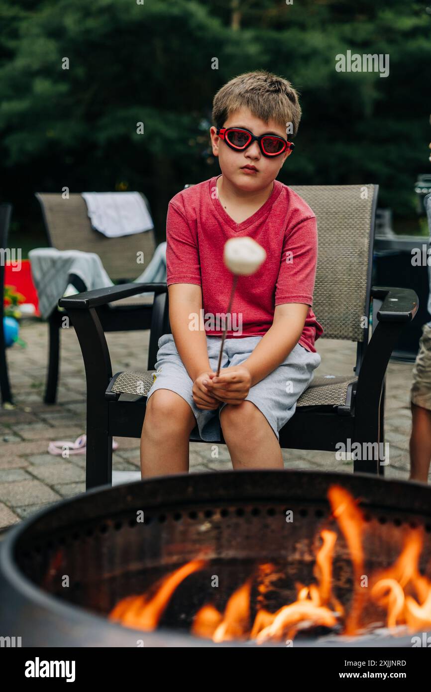 Ragazzo che indossa occhiali da sole rossi che arrostisce un marshmallow Foto Stock