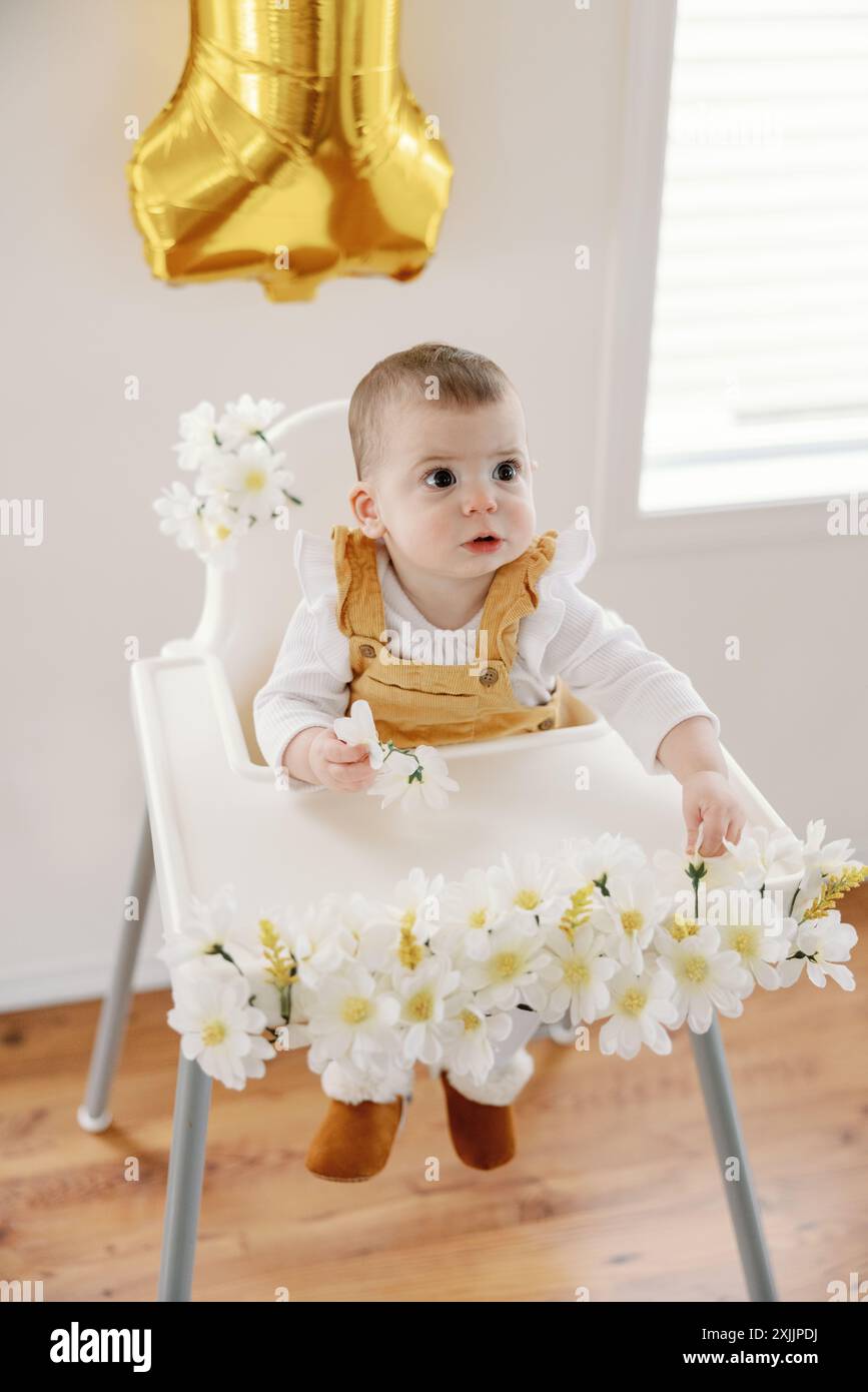 Il primo compleanno del bambino con palloncino dorato e seggiolone floreale Foto Stock