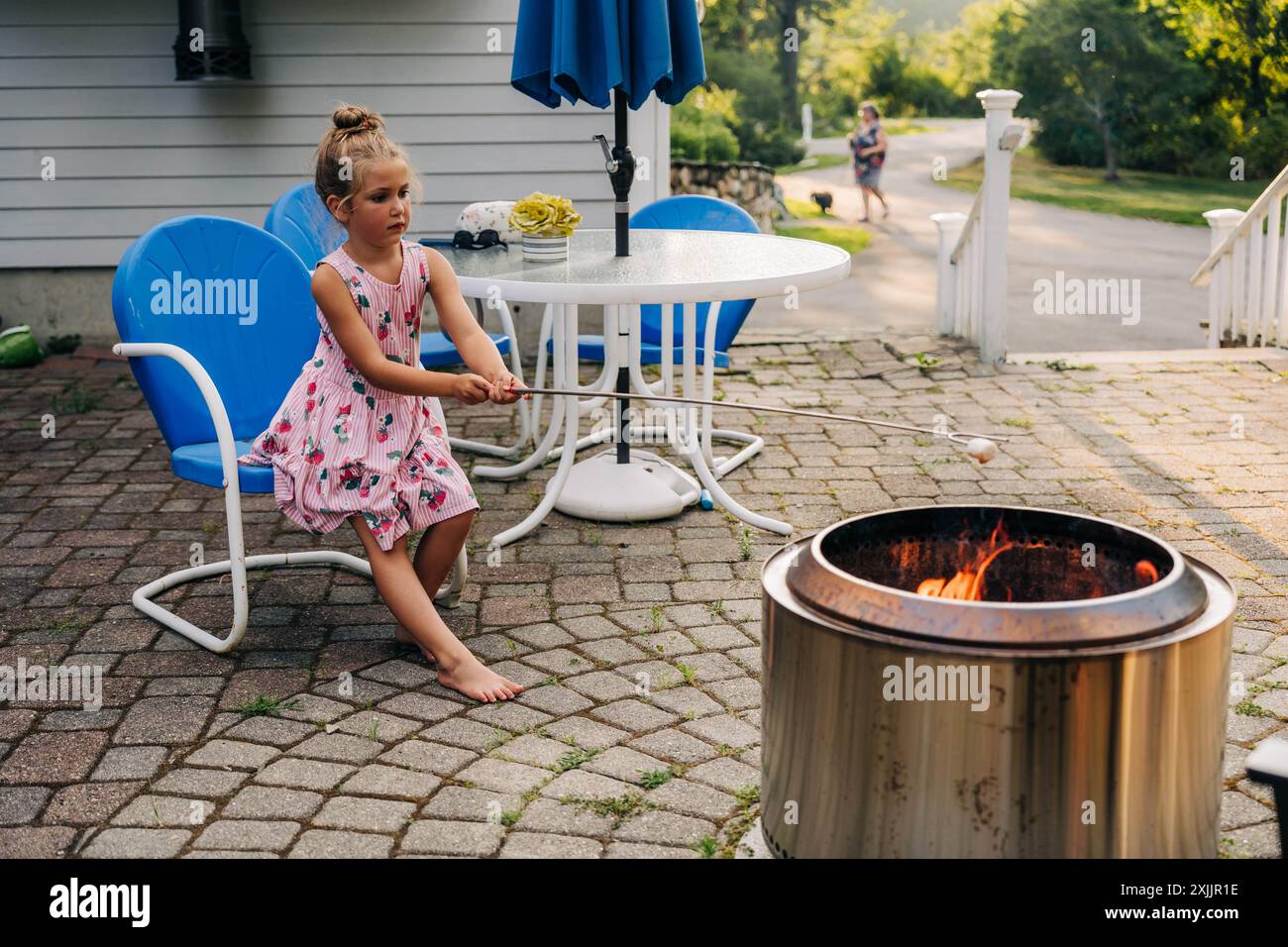 Ragazza che arrostisce il marshmallow sul pozzo del fuoco nel patio del cortile Foto Stock