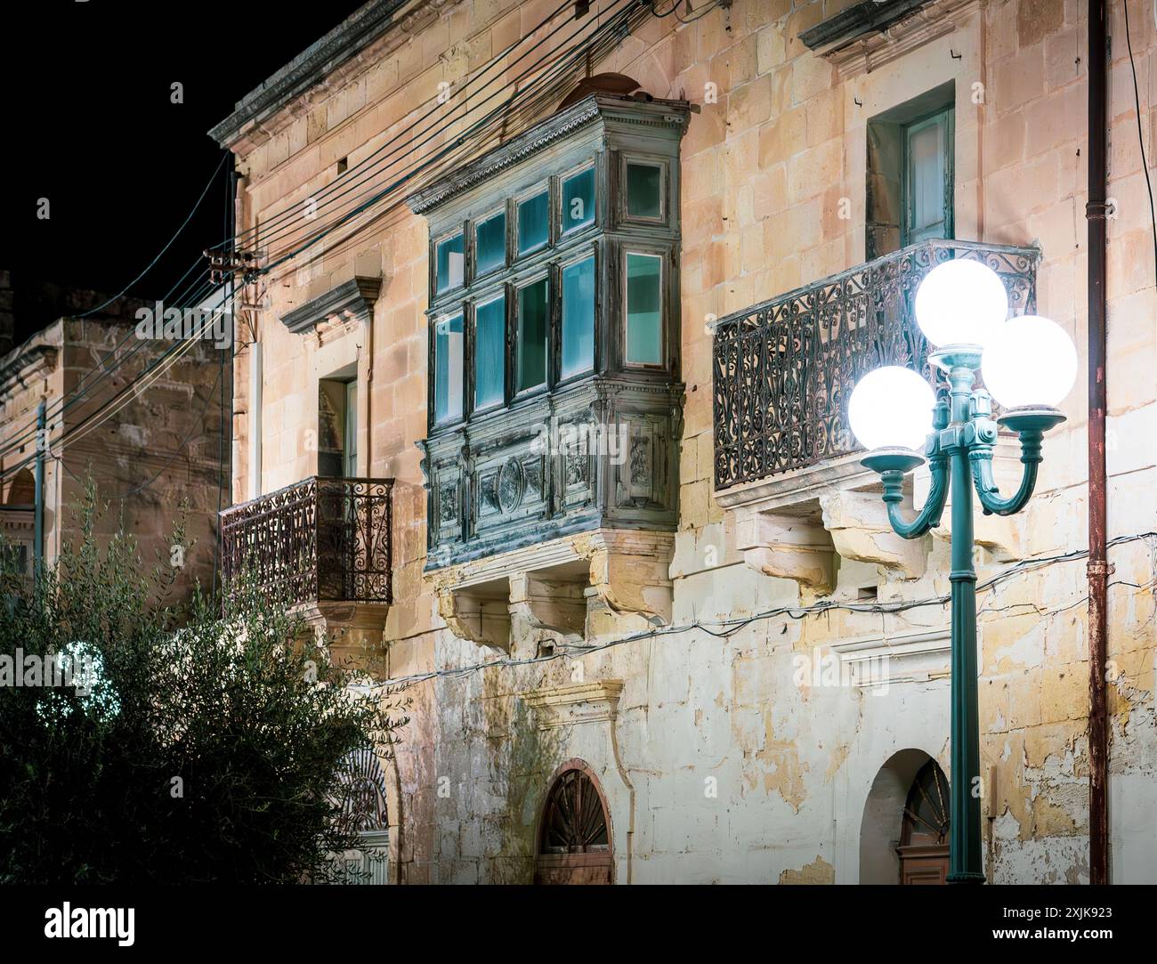 La facciata dell'edificio storico illuminato presenta balconi ornati e una lampada da strada d'epoca di notte. Evoca un senso di nostalgia e fascino del vecchio mondo. Foto Stock