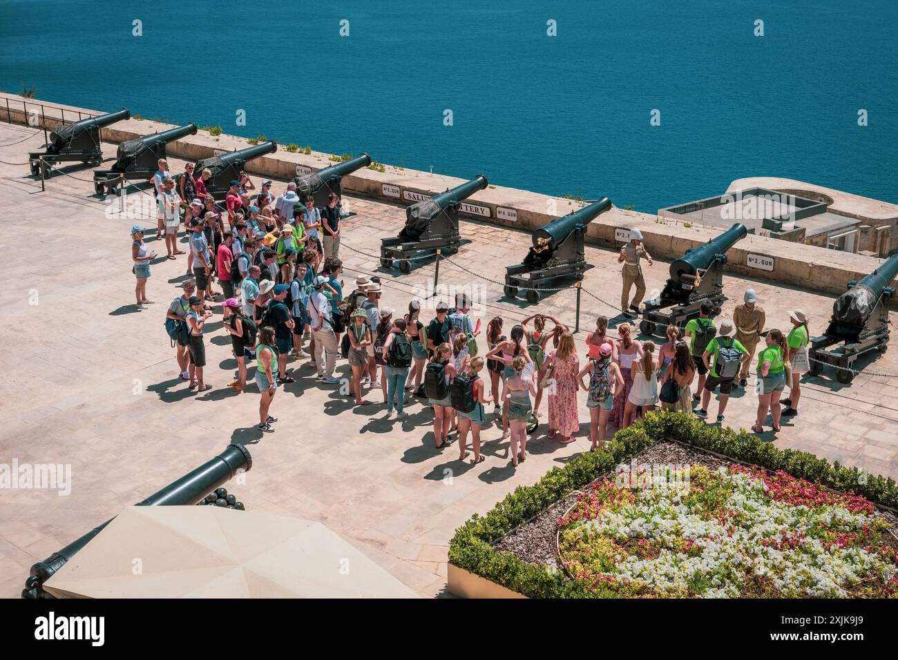 Un gruppo di turisti si riunisce intorno ai cannoni storici durante un tour guidato in riva al mare in una giornata di sole. Foto Stock