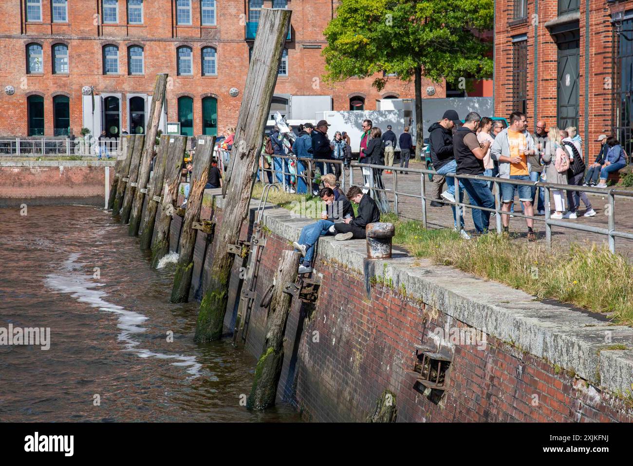 Persone che si rilassano e si godono bevande sulla riva del fiume Elba fuori Fischauktionshalle la domenica mattina ad Amburgo, Germania Foto Stock