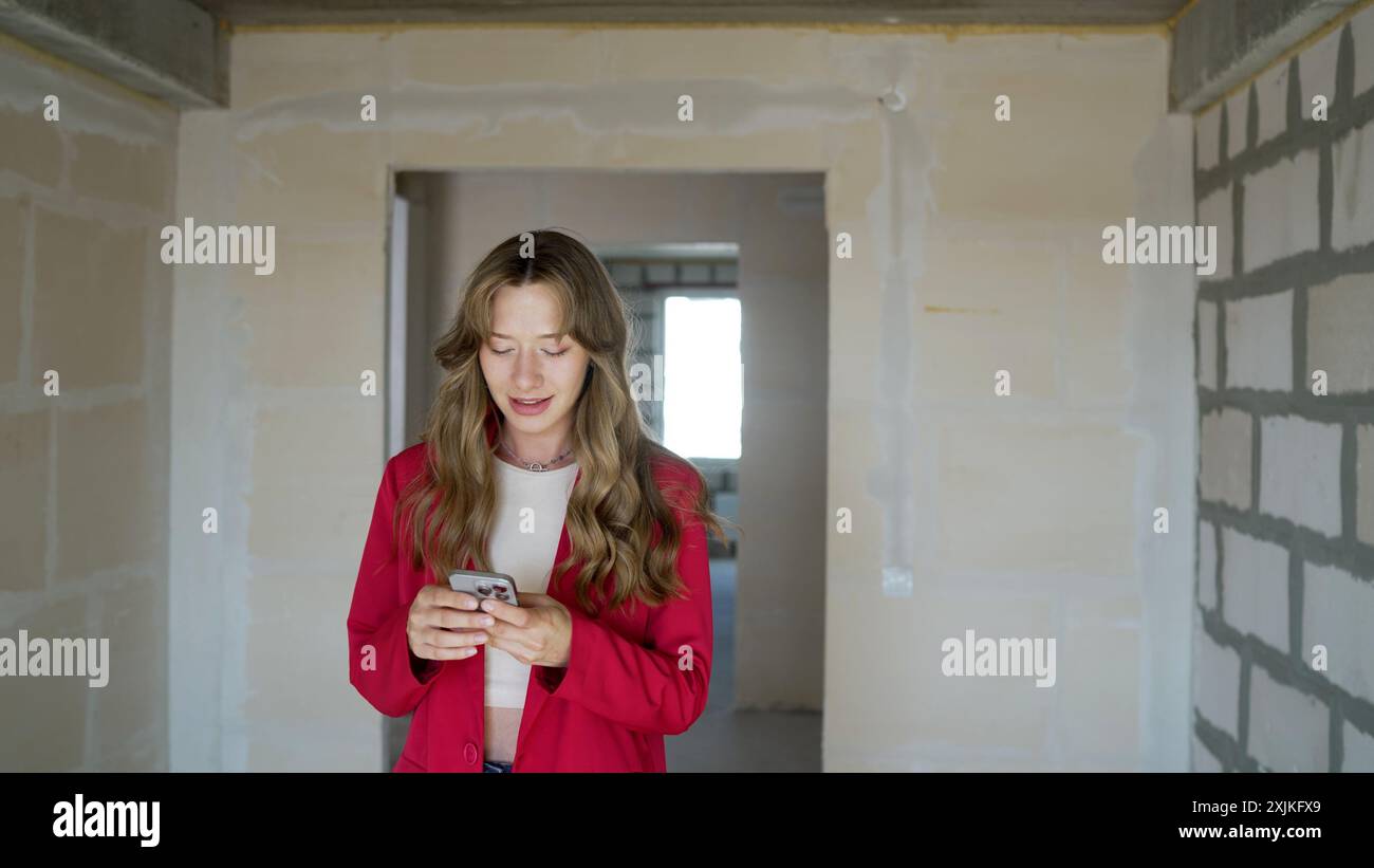 Una ragazza scrive SMS su uno smartphone al chiuso. Ragazza che tiene un telefono, primo piano, che cerca al telefono. Una ragazza irriconoscibile tiene il telefono con entrambi Foto Stock