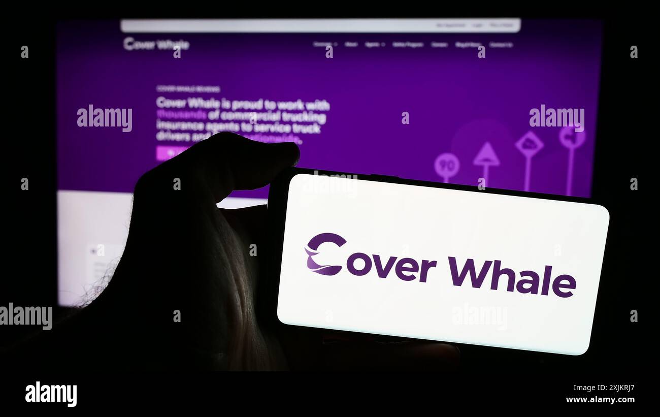 La persona che possiede uno smartphone con il logo della società statunitense copre Whale Insurance Solutions Inc. Davanti al sito Web. Mettere a fuoco il display del telefono. Foto Stock