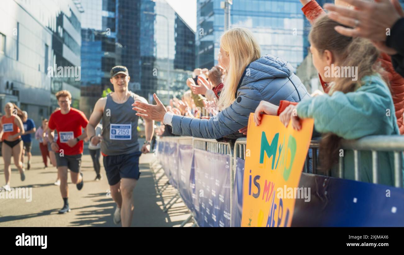 Il pubblico della maratona sostiene e sostiene i propri cari che partecipano alla gara: Atletica maschile Marathon Runner che dà un High Five a un membro della famiglia femminile nel pubblico durante la corsa Foto Stock