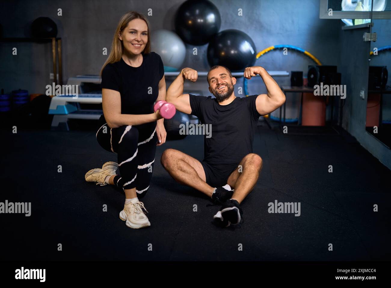 Felice coppia atletica che si flette i muscoli dopo un duro allenamento in palestra e guarda la macchina fotografica, sorridendo. Foto Stock
