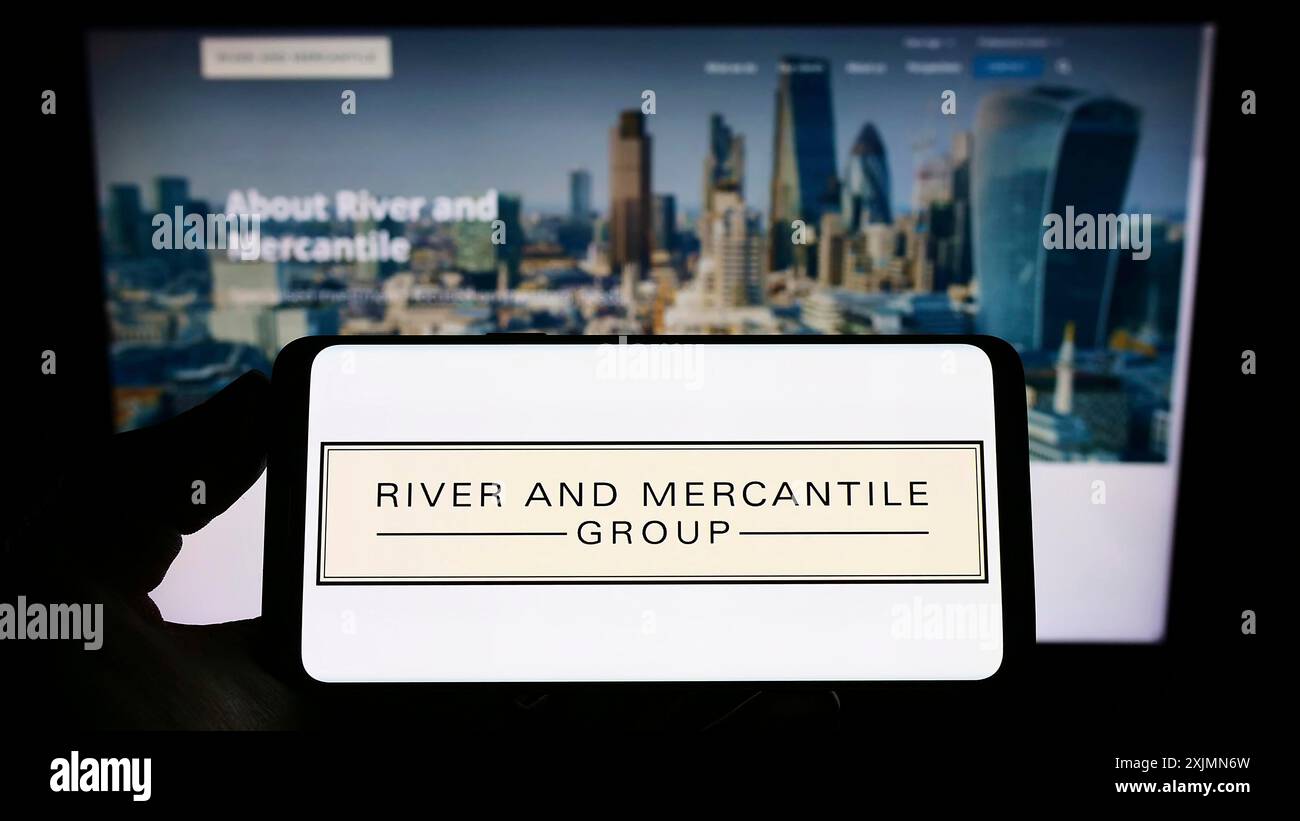 Smartphone con logo dell'azienda River and Mercantile Group Limited sullo schermo davanti al sito Web. Mettere a fuoco il display del telefono Foto Stock