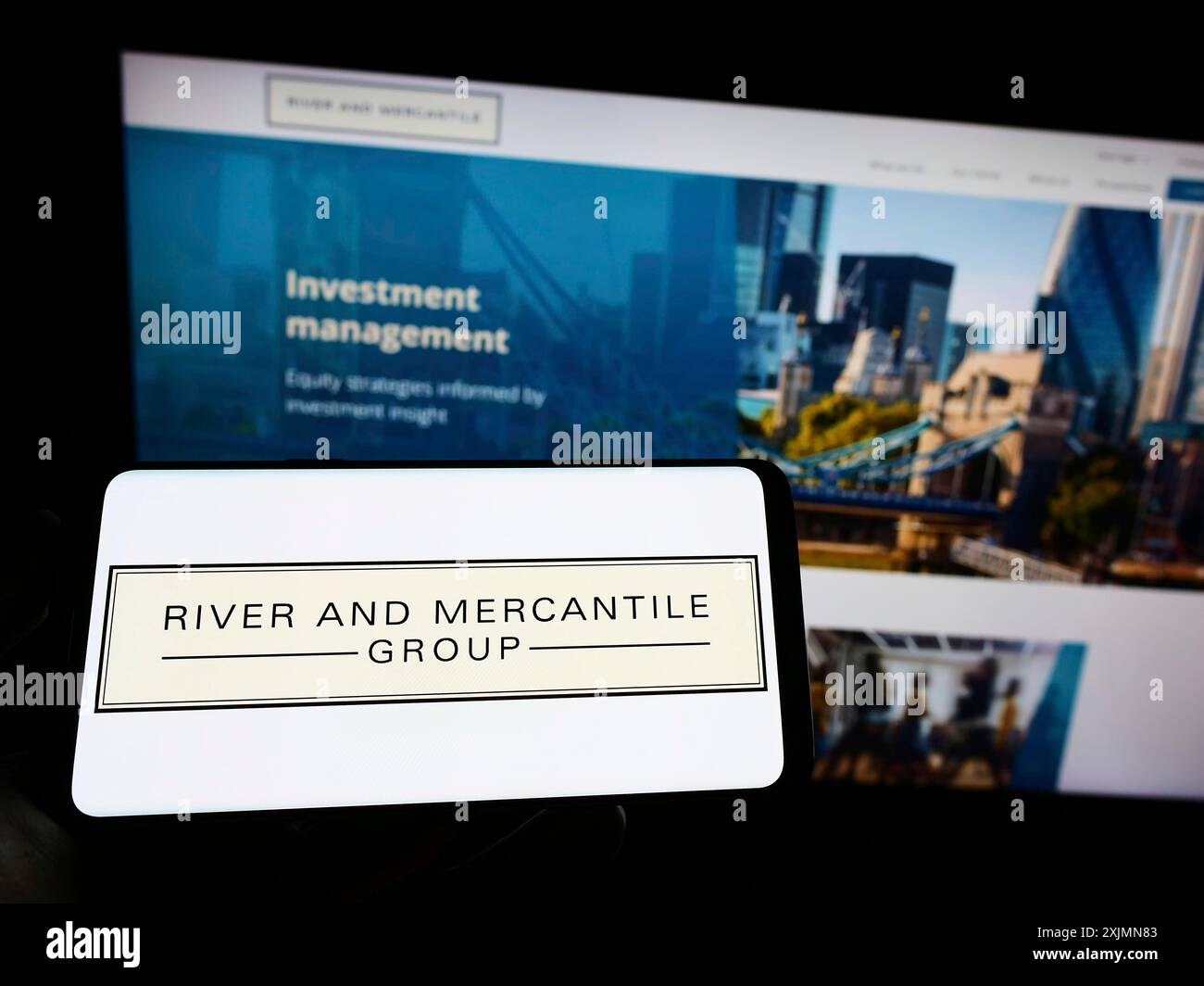 Telefono cellulare con logo della società River and Mercantile Group Limited sullo schermo di fronte alla pagina Web aziendale. Mettere a fuoco il display del telefono Foto Stock