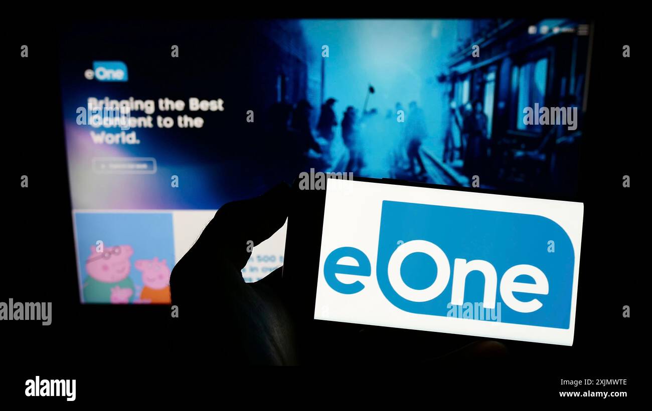 Stoccarda, Germania, 12-02-2022: Persona che detiene un cellulare con il logo della società canadese di intrattenimento eOne Ltd. Sullo schermo davanti all'azienda Foto Stock