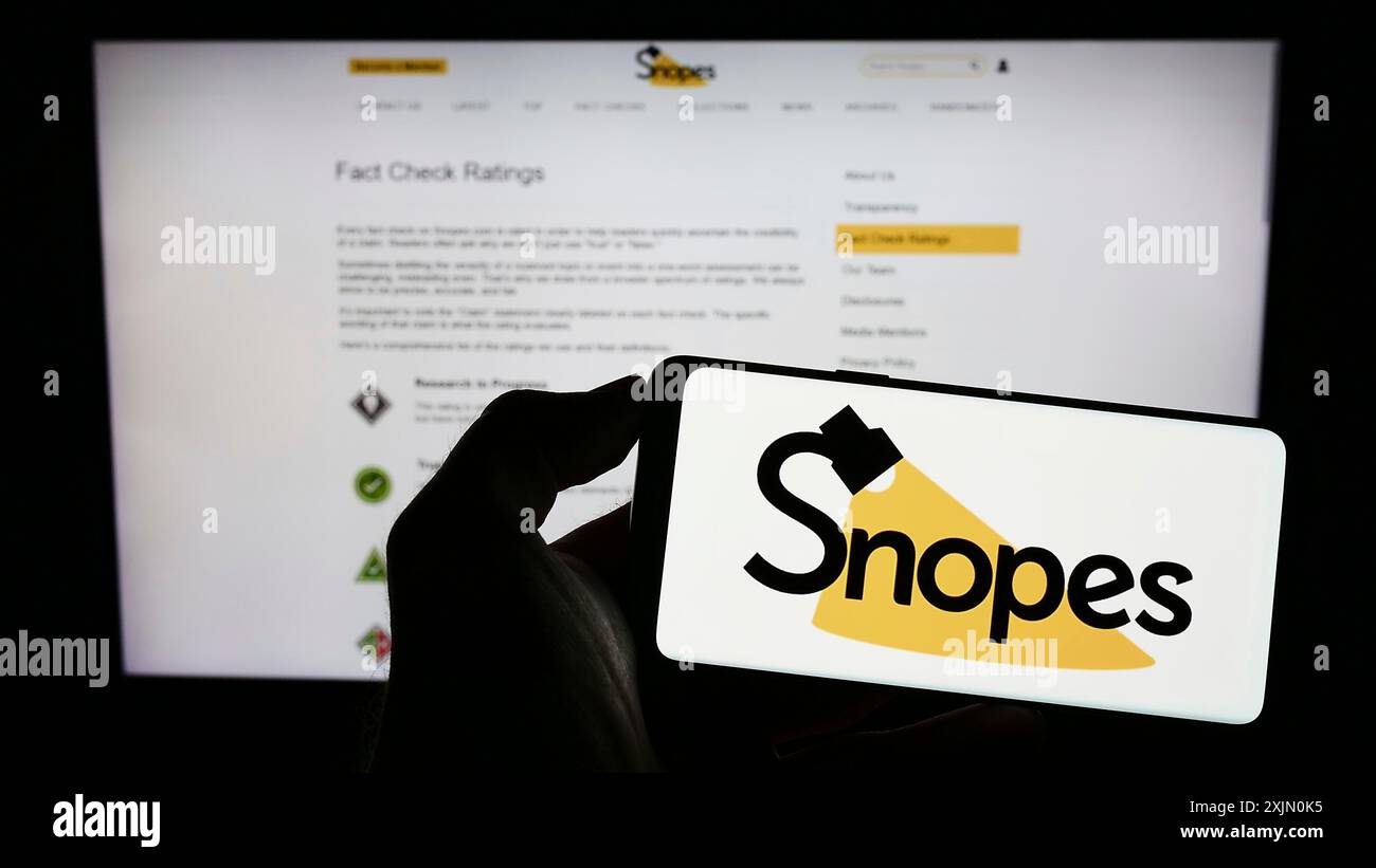 Stoccarda, Germania, 01-14-2023: Persona che tiene un cellulare con il logo della piattaforma di controllo dei fatti degli Stati Uniti Snopes Media Group Inc. Sullo schermo di fronte Foto Stock