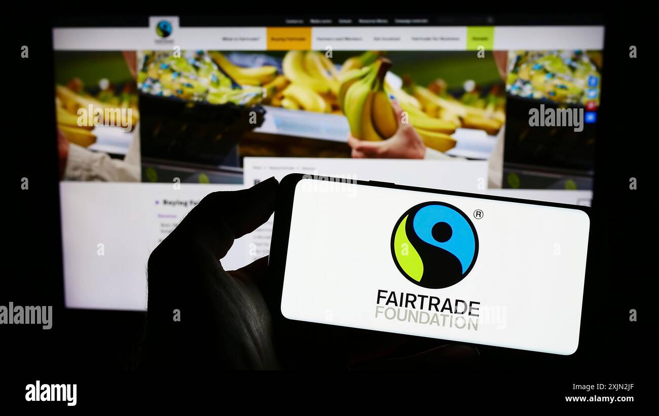 Stoccarda, Germania, 03-11-2023: Persona che detiene un telefono cellulare con il logo dell'organizzazione benefica The Fairtrade Foundation sullo schermo di fronte al web Foto Stock