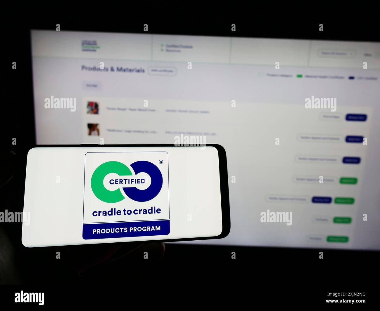 Stoccarda, Germania, 03-11-2023: Persona che tiene il cellulare con il logo dell'etichetta ambientale Cradle to Cradle certificata sullo schermo davanti alla pagina Web. Foto Stock