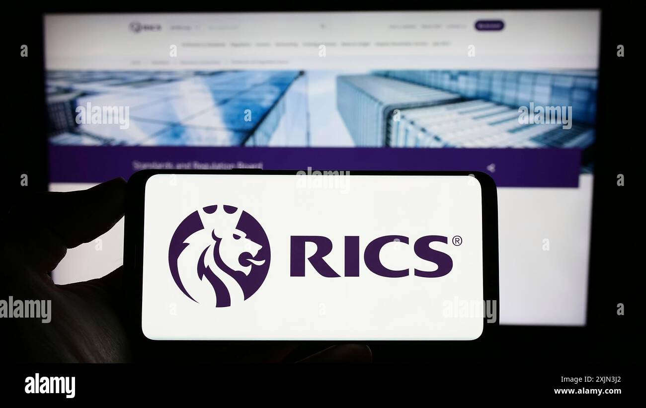 Stoccarda, Germania, 03-18-2023: Persona che detiene un cellulare con il logo della Royal Institution of Chartered Surveyors (RICS) sullo schermo davanti alla pagina web. Foto Stock