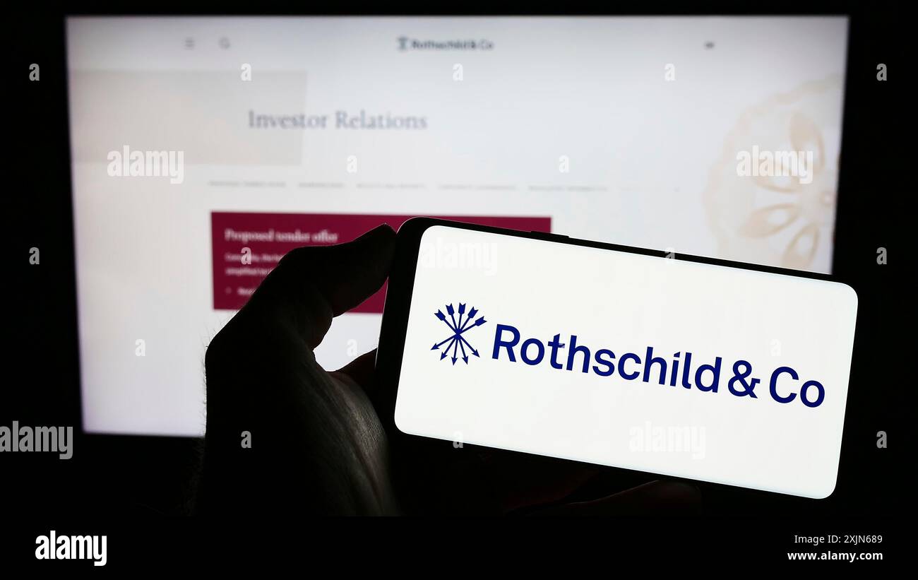 Stoccarda, Germania, 03-31-2023: Persona che tiene il cellulare con il logo della società di servizi finanziari Rothschild Co sullo schermo davanti all'azienda Foto Stock