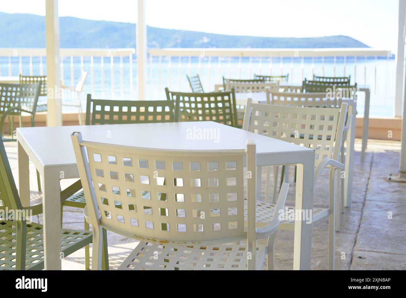 Tavoli e sedie vuoti di un caffè sulla strada situato sulla costa del mare. Posti a sedere gratuiti sulla terrazza del caffè di mattina presto. Foto Stock