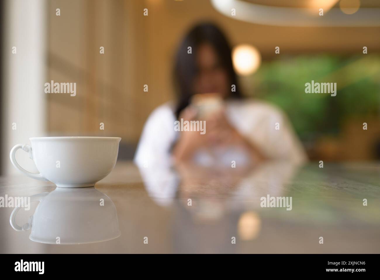 Tazza di caffè in primo piano con una giovane donna tailandese sorridente in background Foto Stock