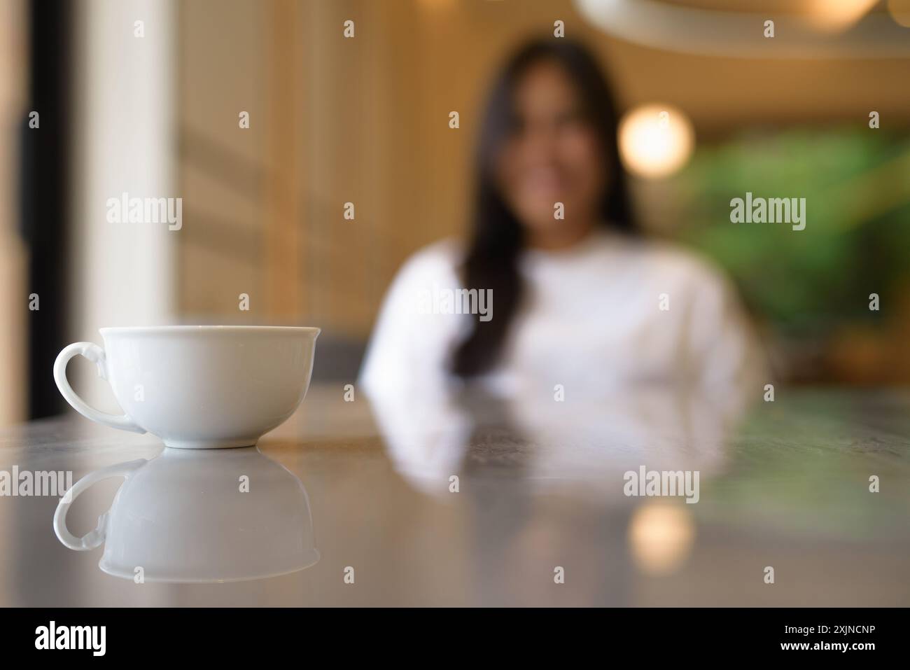 Tazza di caffè in primo piano con una giovane donna tailandese sorridente in background Foto Stock
