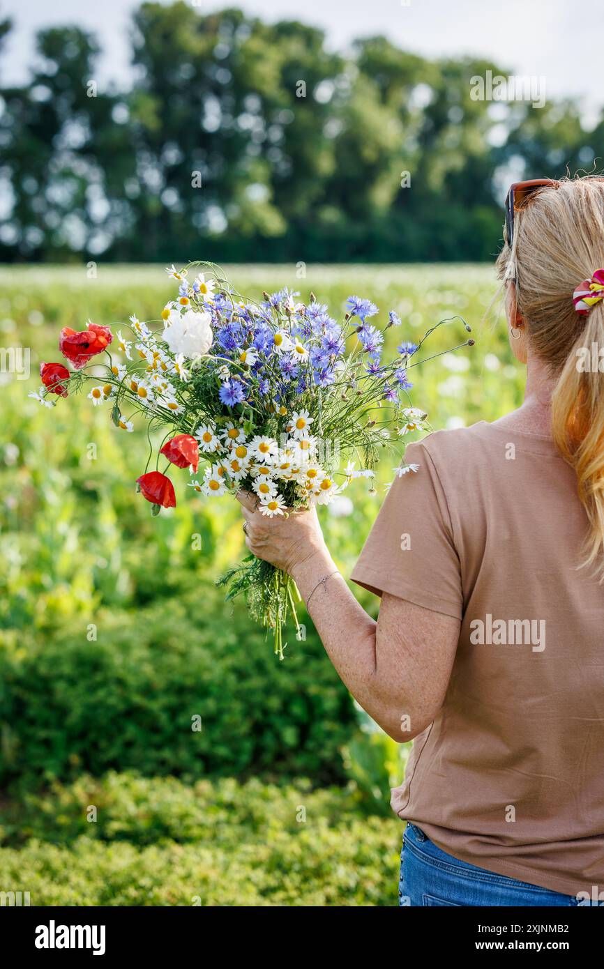 Donna con un bouquet di fiori selvatici colorato in un lussureggiante campo estivo. Temi della natura, del relax e della bellezza botanica Foto Stock