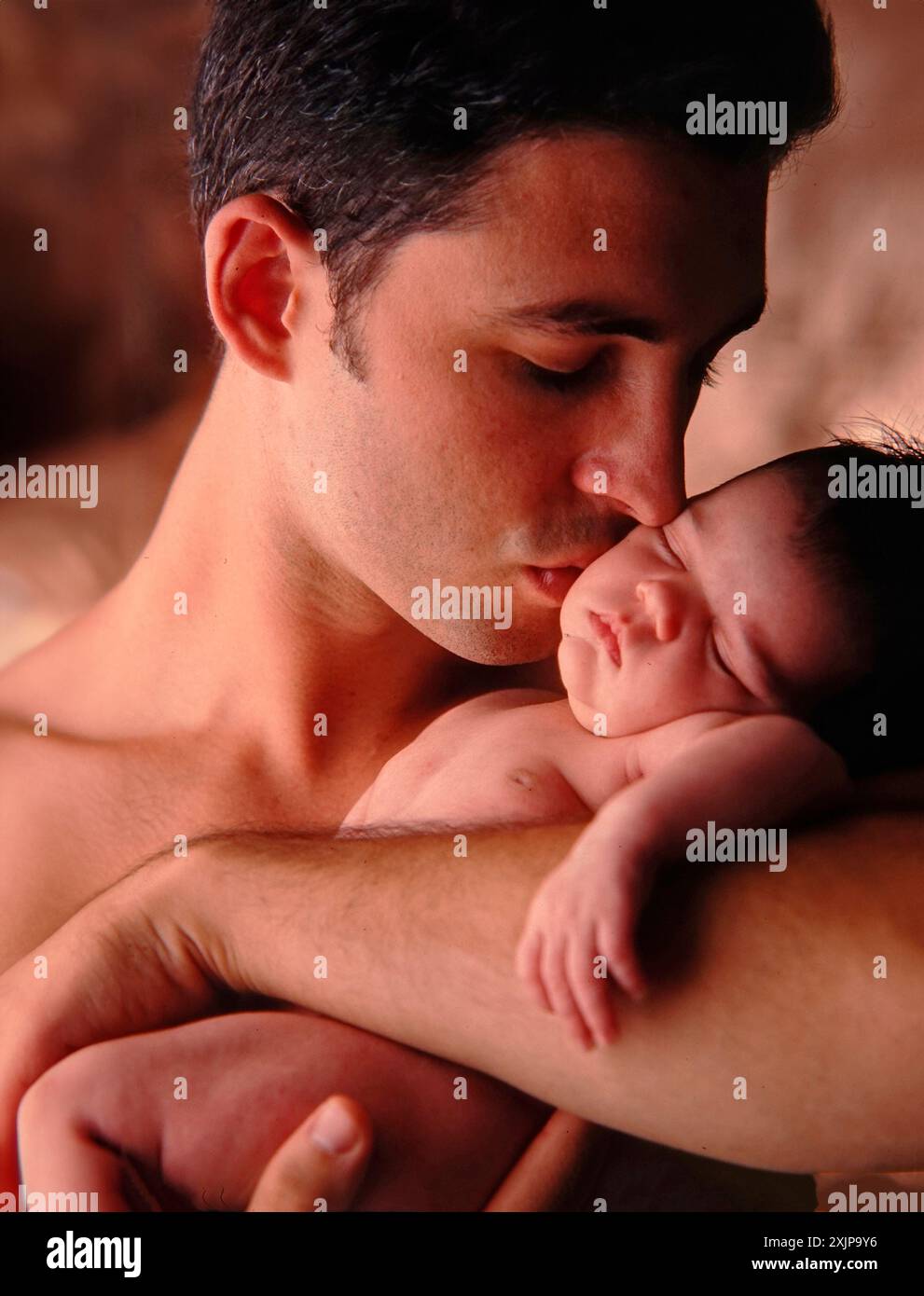 Un padre culla dolcemente il suo neonato tra le braccia, il suo viso si rivolge verso il bambino mentre bacia la fronte. Il bambino sta dormendo in quello del padre Foto Stock