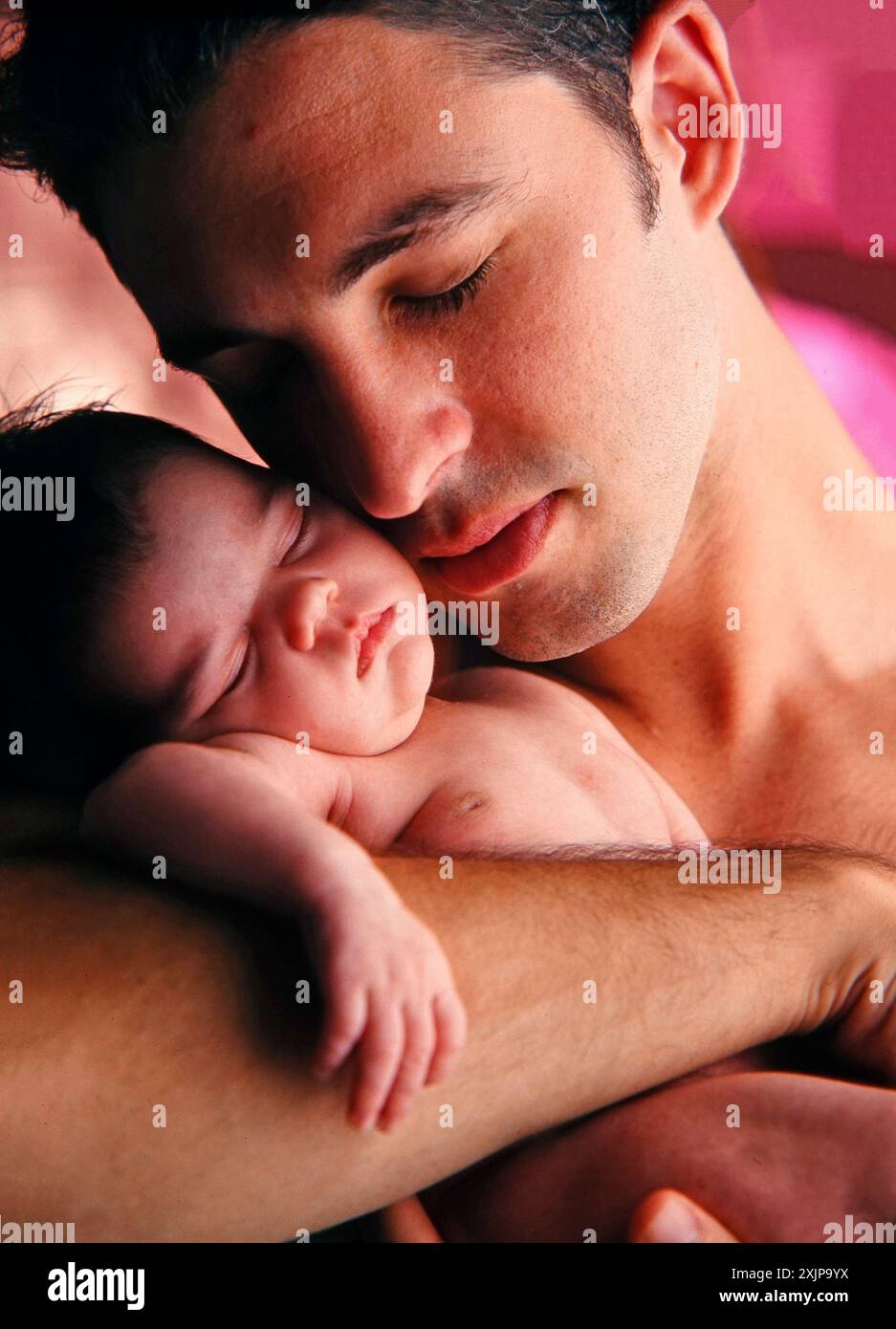 Un padre tiene in braccio il suo bambino appena nato, che dorme pacificamente tra le sue braccia. Gli occhi del padre sono chiusi, e lui ha un'espressione gentile sul suo viso come h Foto Stock