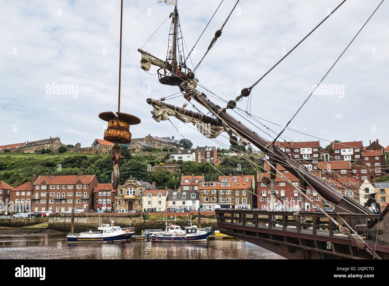 Un albero di una nave storica con una città costiera sullo sfondo. La città presenta tradizionali case in mattoni e un lungomare con piccole barche Foto Stock