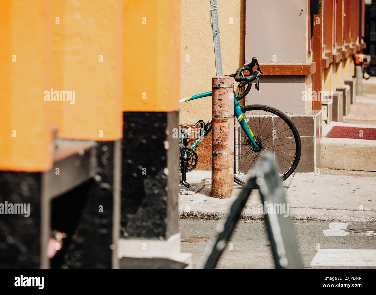 Una bicicletta colorata è bloccata su un palo su una strada della città, parzialmente oscurata da una struttura nera e gialla a Philly Foto Stock