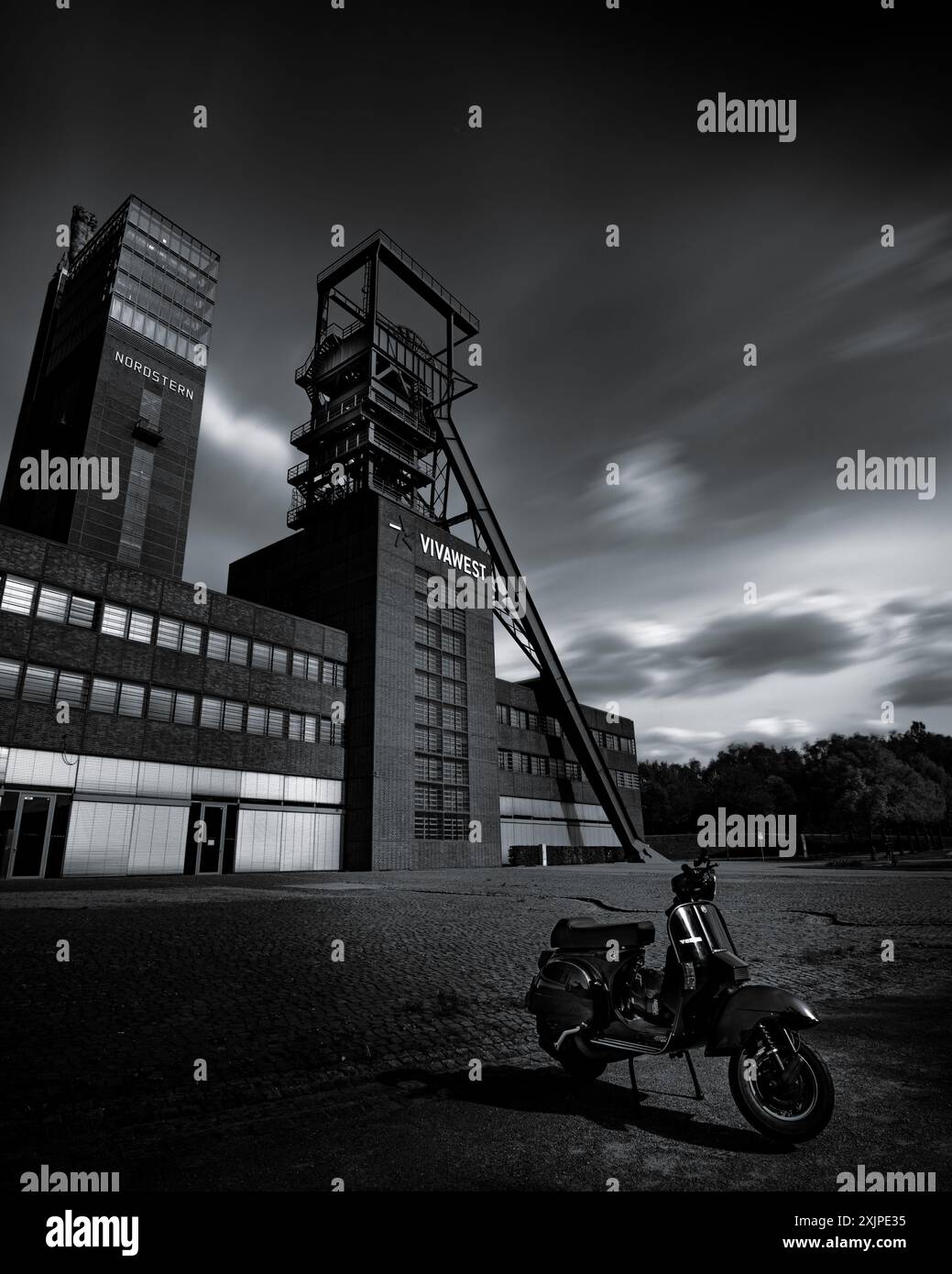 Una foto verticale in scala di grigi di una moto parcheggiata di fronte al museo di storia Nordstern nel Polar Star Park, Gelsenkirchen, Germania Foto Stock
