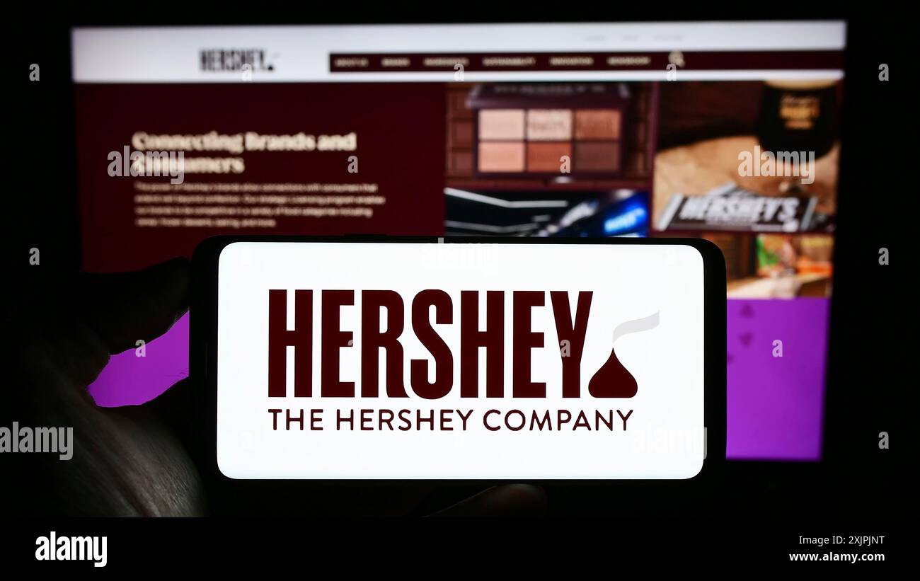 Stoccarda, Germania, 07-02-2023: Persona con smartphone con logo del settore alimentare statunitense The Hershey Company sullo schermo di fronte al sito web. Concentrati su Foto Stock