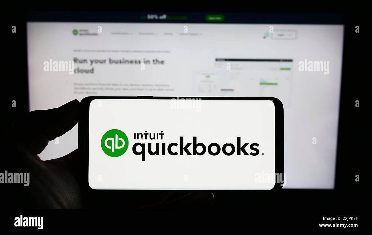 Stoccarda, Germania, 07-09-2023: Persona con smartphone con logo del software di contabilità QuickBooks sullo schermo di fronte al sito web. Concentrati sul telefono Foto Stock